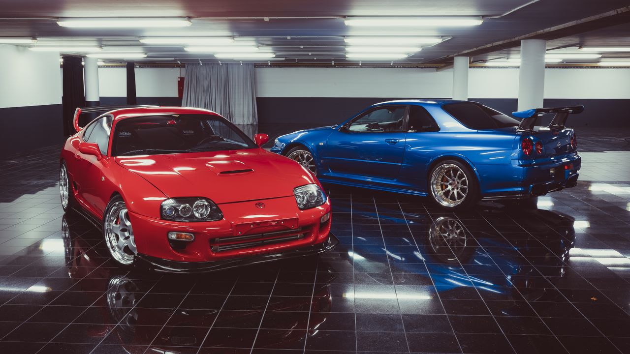 Red Toyota Supra and blue Nissan Skyline showcased in an elegant indoor garage setting.
